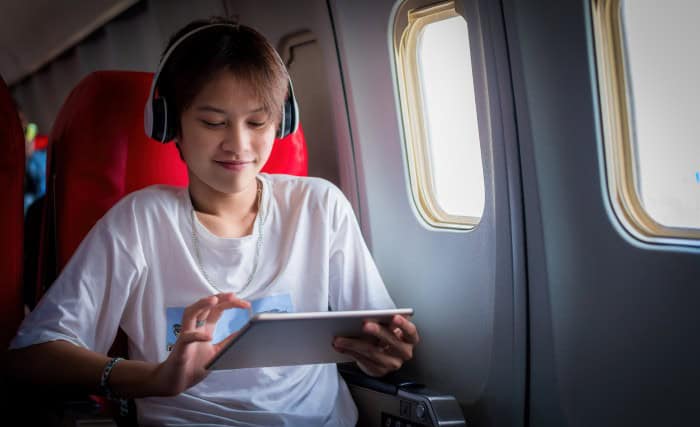 oung happiness tourist teenager passenger flight seat near window using tablet app relax litsening music bluetooth headphones noise-cancelling using wifi internet connection on board.